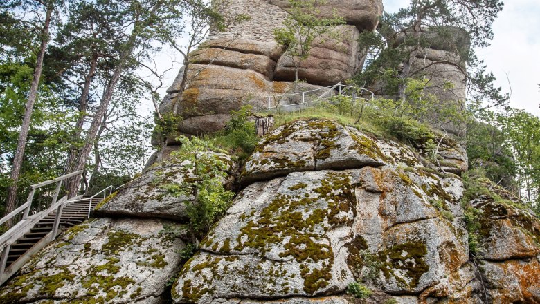 Burgruine Arbesbach, © Waldviertel Tourismus, Erwin Haiden Ein Radfahrer lehnt an einem Baumstumpf vor einem hohen, felsigen Turm in einer bewaldeten Umgebung.