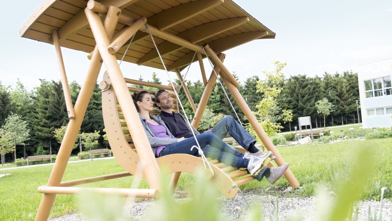 Entspannung, © Xundheitswelt Ein Paar entspannt auf einer großen Holzschaukel im Freien.