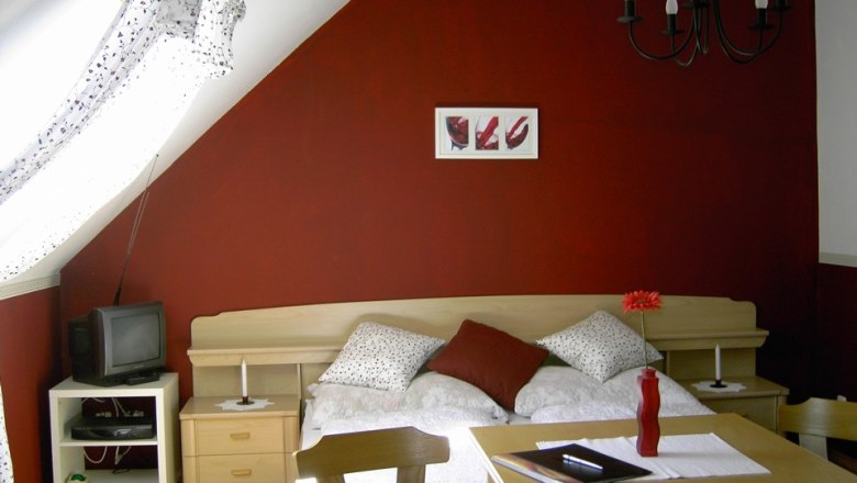 Appartement ROT, © Weingut Kamauf Gemütliches Schlafzimmer mit roter Wand, Bett, Tisch und Fernseher.