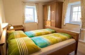 Schlafzimmer - Landhaus Lunkowitz, © Benjamin Butschell Gemütliches Schlafzimmer mit Holzmöbeln und bunten Bettbezügen.