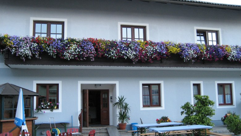 Gasthof Lichtenwallner, © Gasthof Lichtenwallner Gasthof mit blauer Fassade, Blumenkästen am Balkon und Biergartenmöbeln im Vordergrund.