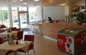 Cafeteria im Neuro Rehab Allentsteig, © Stadtgemeinde Allentsteig Innenansicht eines Cafés mit roten Stühlen, Holztresen und Eiskühltruhe.