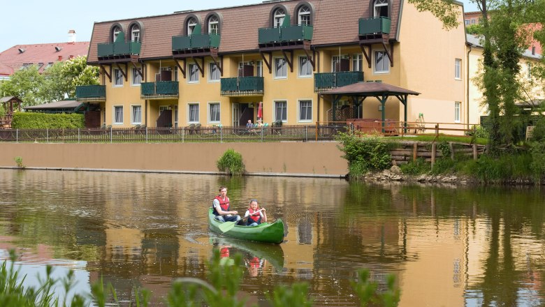 Kanufahren Hotel Thaya, © Hotel Thaya Zwei Personen in einem Kanu auf einem Fluss vor einem gelben Hotel.