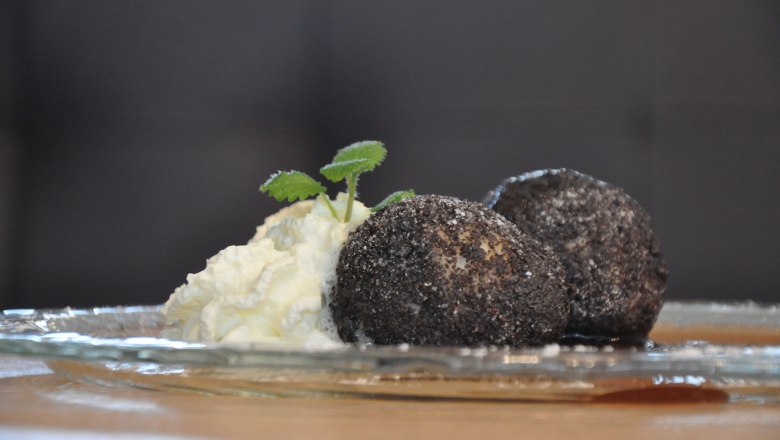 Mohnknödel, © Café Pension Kristall Zwei Mohnknödel mit Sahne und Minzblättern auf einem Glasteller.