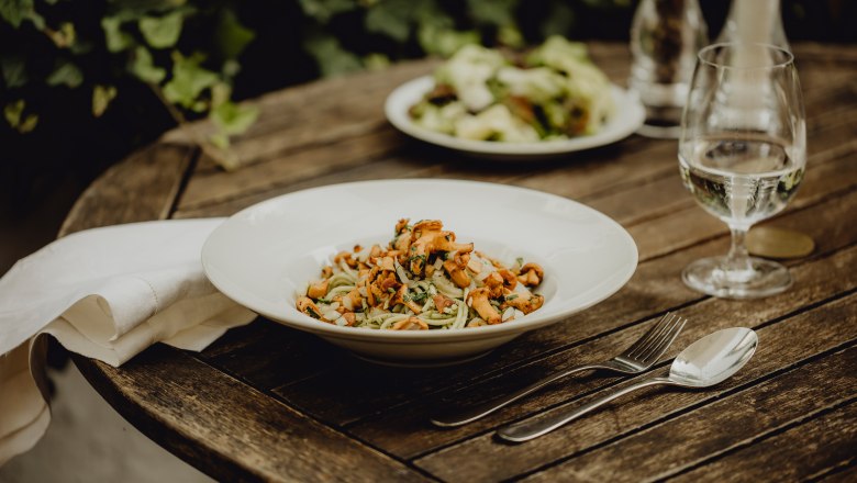 Pesto chanterelle pasta, © Niederösterreich Werbung/Sophie Menegaldo A plate of pesto chanterelle pasta on a wooden table, cutlery and a glass of water next to it.