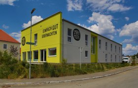 Smart Motel Außenansicht, © Smart Motel GmbH Außenansicht eines modernen, zweistöckigen Motels mit gelber Fassade und der Aufschrift 'Einfach gut übernachten'.