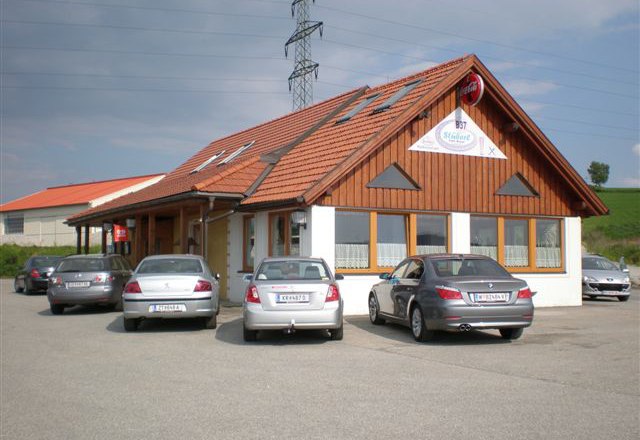 B37 Stüberl, © MG Rfd Ein Restaurant mit Holzfassade und mehreren geparkten Autos davor.