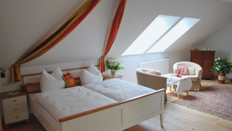 Premium bon-vivant rooms Kibitzhof, © Kibitzhof Cozy bedroom with double bed, armchairs and table under a sloping roof.