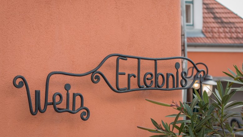 LIebevolle Details außen wie innen, © Alte Schmiede Schönberg Metallschild mit der Aufschrift 'Wein Erlebnis' an einer orangefarbenen Wand.