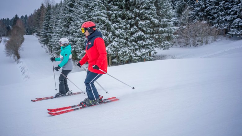 Schidorf Kirchbach, © Waldviertel Tourismus, Robert Herbst Zwei Skifahrer auf einer verschneiten Piste, umgeben von schneebedeckten Bäumen.