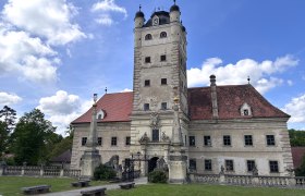 Schloss Greillenstein, © "Natur im Garten" Schloss Greillenstein mit Turm und rotem Dach vor blauem Himmel.