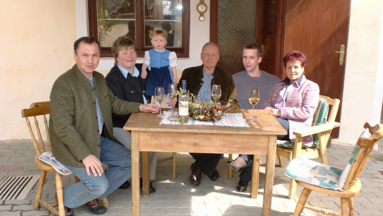 Familienbetrieb, © Familie Arocker Eine Familie sitzt an einem Holztisch im Freien und trinkt Wein.