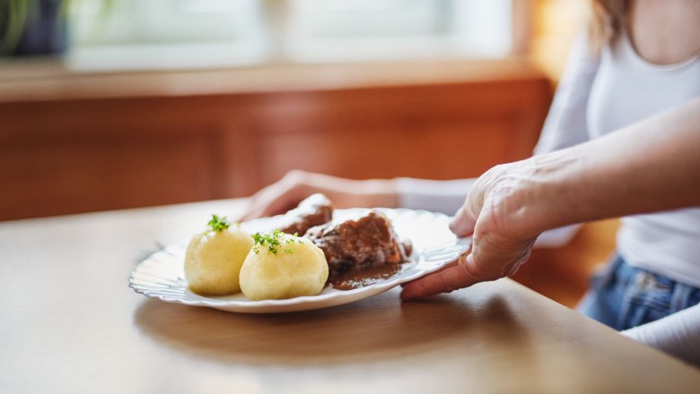 Waldviertler Erdäpfelknödel, © Waldviertel Tourismus, Gerhard Wasserbauer Ein Teller mit zwei Waldvierter Erdäpfelknödeln und Fleisch in Soße wird auf einem Tisch serviert.