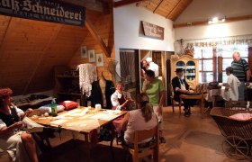 Heimatmuseum Kautzen, © Heimatmuseum Kautzen Innenansicht eines Heimatmuseums mit Menschen in traditioneller Kleidung, die handwerkliche Arbeiten zeigen.