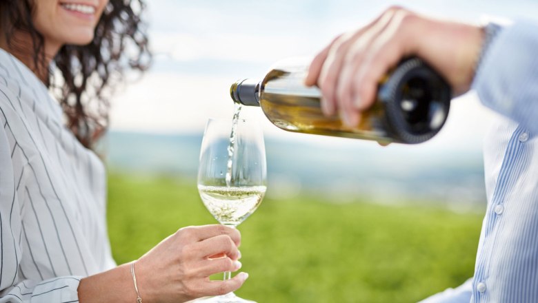 Ursin House, © © Waldviertel Tourismus, Gerhard Wasserbauer A person pours white wine into a glass held by another person, with a vineyard in the background.
