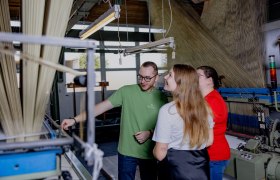 Führung durch die Produktion, © Waldviertel Tourismus, Matthias Streibel Drei Personen in einer Textilfabrik betrachten eine Maschine.