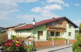 Ferienbauernhof Schierhuber, © MG Sallingberg Ein Ferienbauernhof mit grünem Anstrich und Holzbalkon, umgeben von einem Holzzaun und Blumen im Vordergrund.