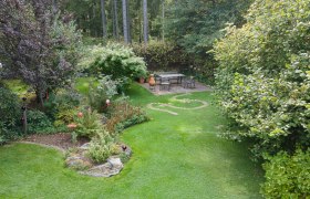 einblick-in-den-garten, © Dagmar Scheucher Ein gepflegter Garten mit Rasen, Bäumen und einem Sitzbereich auf einer Terrasse.