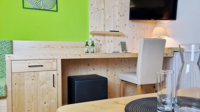 Doppelzimmer, © Café-Pension Kristall, Julian Weber Ein Hotelzimmer mit Holzmöbeln, einem Schreibtisch, einem Fernseher an der Wand und einer grünen Wanddekoration.