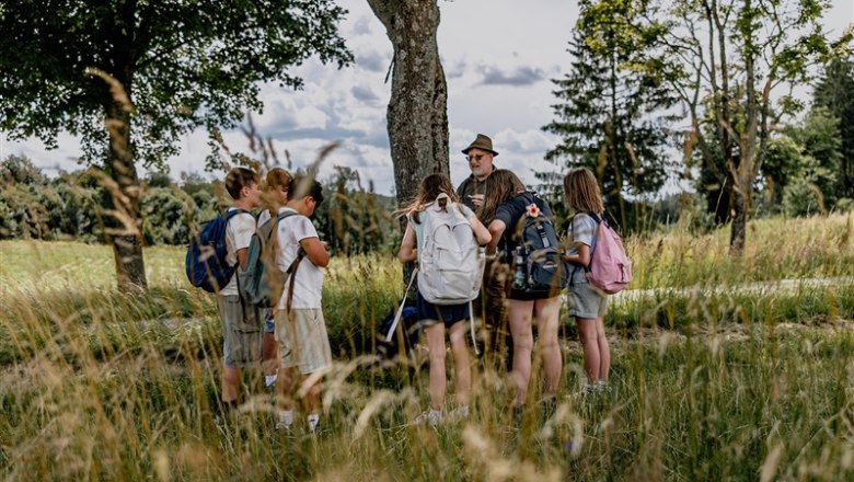 Waldschule Waldviertel, © Waldviertel Tourismus, Matthias Streibel Gruppe von Kindern mit Rucksäcken und einem Erwachsenen im Freien, umgeben von Bäumen und Gras.