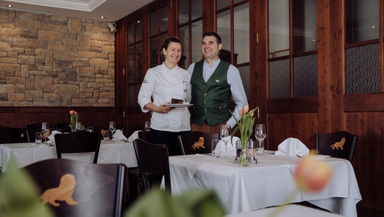 Chefköchin Margit und Biersommelier Andreas Frey, © Niederösterreich Werbung/thecreatingclick.com Eine Chefköchin und ein Mann in traditioneller Kleidung stehen lächelnd in einem eleganten Restaurant.