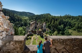 Ruine Kollmitz, © Waldviertel Tourismus, Studio Kerschbaum Zwei Personen betrachten die Ruine Kollmitz von einer Mauer aus, umgeben von einem dichten Wald und blauem Himmel.