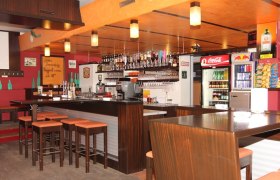 Auberg Pub_01, © Auberg Pub Innenansicht einer Bar mit Holzmöbeln, Barhockern und Getränken.