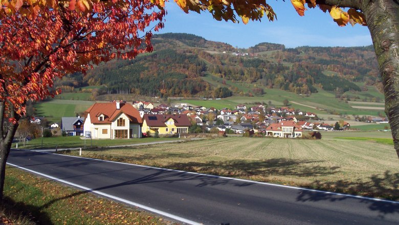 Laimbach am Ostrong, © Gemeinde Münichreith-Laimbach Herbstlandschaft mit Dorf und Hügeln im Hintergrund, Laubbäume mit bunten Blättern im Vordergrund.
