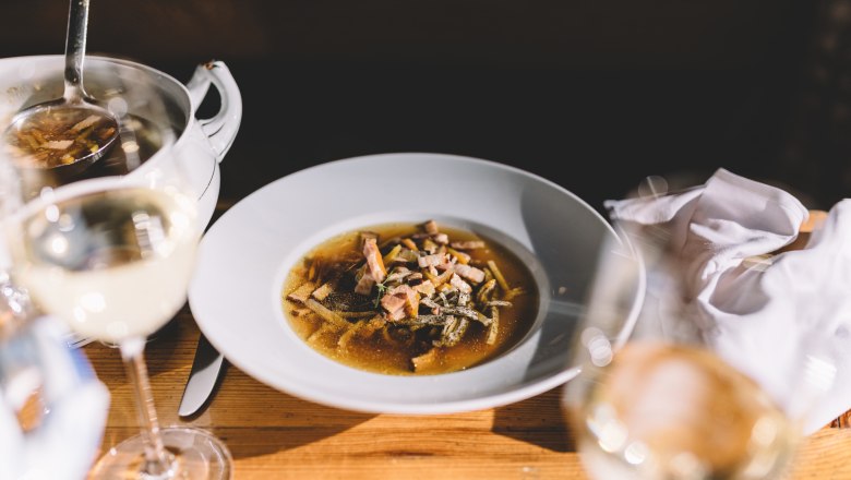 Roggenbiersuppe mit Mohnfrittaten, © Niederösterreich Werbung/Mara Hohla Ein Teller mit Roggenbiersuppe und Mohnfrittaten auf einem Holztisch, daneben ein Glas Weißwein.