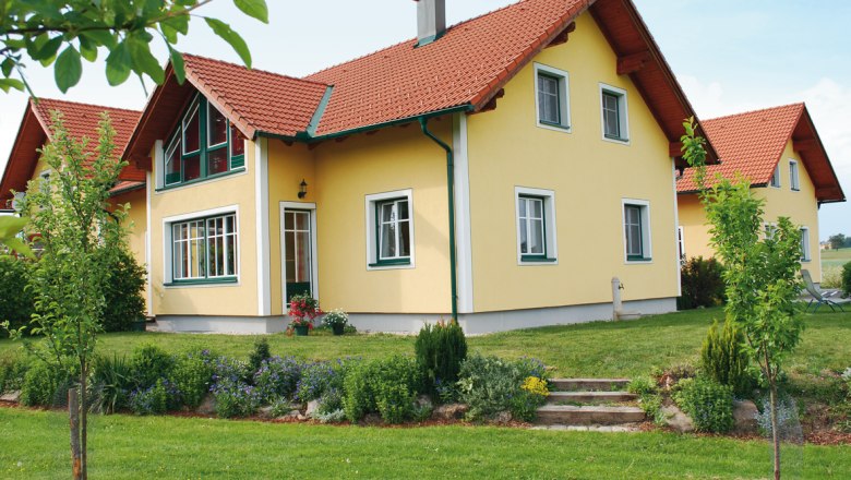 Kibitzhof, © Kibitzhof Gelbes Einfamilienhaus mit rotem Dach und gepflegtem Garten.