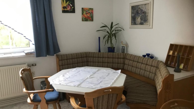 Esszimmer, © Ferienwohnung Meindl-Grübling Eckbank in einer Küche mit Tisch und Stühlen, dekoriert mit Pflanzen und Bildern an der Wand.