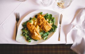 Wald4tler Bio-Karpfenfilet in Roggen-Bierteig gebacken, © Niederösterreich Werbung/Mara Hohla Ein Teller mit gebackenem Karpfenfilet auf Feldsalat und Kartoffeln, auf einem weiß gedeckten Tisch.