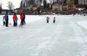 Eislaufen am Stadtsee Allentsteig, © Waldhör Menschen eislaufen auf einem zugefrorenen See in Allentsteig, umgeben von Häusern und Bäumen.