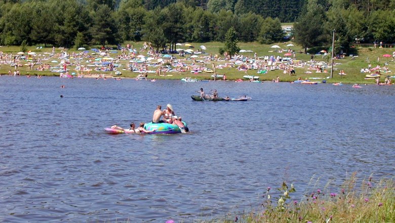 Badestrand Frauenwieserteich, © Gemeinde Langschlag Menschen entspannen am Frauenwieserteich mit Liegen und Sonnenschirmen.
