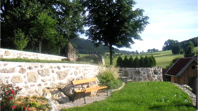 ERLEBNIS: Stein & Garten, © Familie Anderl Ein Garten mit Steinmauer, Bank und Bäumen im Hintergrund.