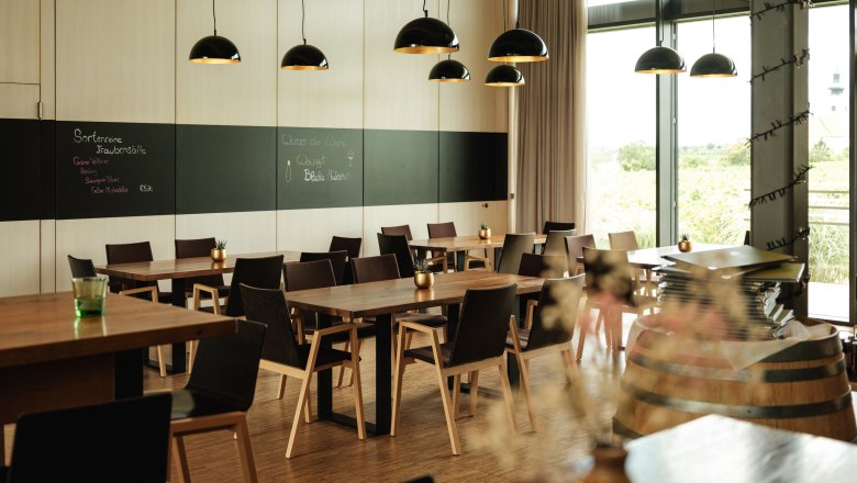 W4, © Weinviertel Tourismus / Michael Reidinger Modernes Restaurant mit Holztischen, schwarzen Stühlen und großen Fenstern. Schwarze Hängelampen und eine Tafel an der Wand.
