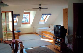 Gästehaus Tüchler, © Gästehaus Tüchler Innenansicht eines gemütlichen Dachgeschosszimmers mit Holzmöbeln, zwei Betten, einem Fernseher und Dachfenstern.