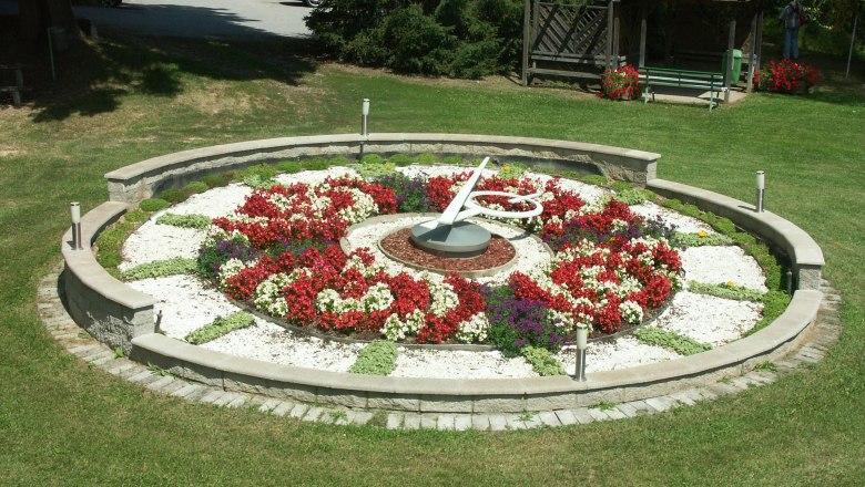 Marktgemeinde Karlstein, © Marktgemeinde Karlstein Blumenuhr in einem Park mit bunten Blumen und einem Pavillon im Hintergrund.