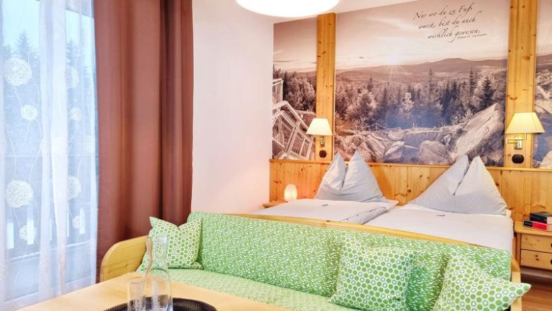 Doppelzimmer, © Café-Pension Kristall, Julian Weber Gemütliches Doppelzimmer mit zwei Betten, grünem Sofa und großem Wandbild einer Landschaft.