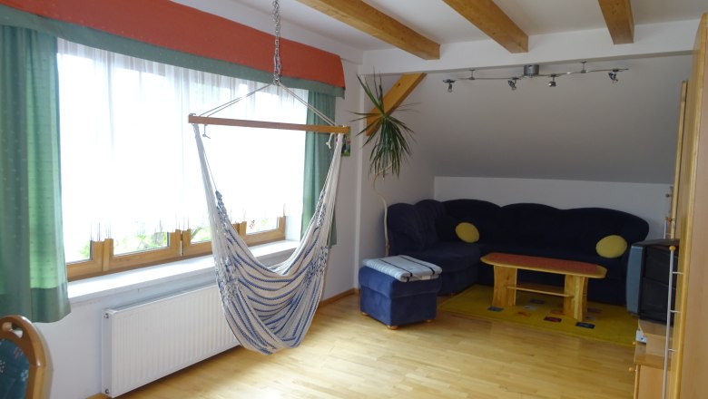 Wohnraum mit TV u Hängesessel, © Maria Bauer Wohnzimmer mit Hängesessel, Sofa, Tisch und TV.