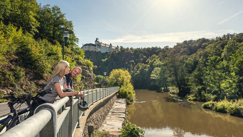 Kamp-Thaya-March Radroute, © Waldviertel Tourismus, Studio Kerschbaum Zwei Personen lehnen an einem Geländer mit Blick auf einen Fluss und eine Burg im Hintergrund.