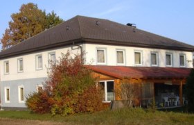 Rasthof Stefanie, © Bernhard Berger Zweistöckiges Gebäude mit grauem Dach und weißen Wänden, umgeben von Bäumen und Sträuchern.