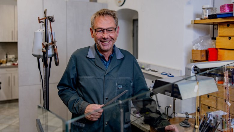 Granitschmuck Reinhart Kartusch, © Waldviertel Tourismus, Matthias Streibel Ein Mann in einer Werkstatt mit Brille und Arbeitskittel, lächelnd, umgeben von Werkzeugen und Schmuck.