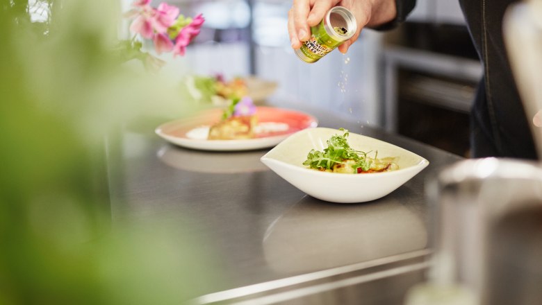 SONNENTOR Leibspeis', © Waldviertel Tourismus, Gerhard Wasserbauer Ein Koch würzt ein Gericht in einer Schüssel mit Kräutern aus einer kleinen Dose.