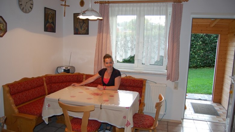 Kitchen apartment, © Poelzl A woman sits at a dining table in a cozy kitchen with a corner bench and red cushions.