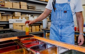 Kerzen färben, © Waldviertel Tourismus, Matthias Streibel Person in Latzhose taucht Kerze in Farbbad.