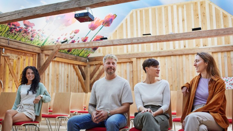 Mohnbauernstadl, © © Waldviertel Tourismus, Gerhard Wasserbauer Vier Personen sitzen in einem Stadl mit einem Deckenbild von Mohnblumen.