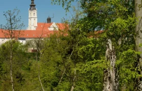 Stiftswald Altenburg, © Matthias Schickhofer Blick auf ein Klostergebäude mit Turm hinter Bäumen im Stiftswald Altenburg.