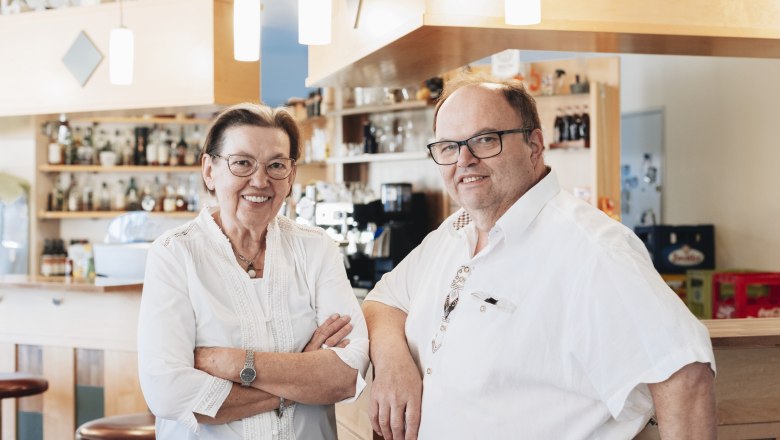 Josef Klang and Aloisia Bachofner, © Niederösterreich Werbung/David Schreiber Two people in a café or bar, smiling, in front of a counter with bottles in the background.
