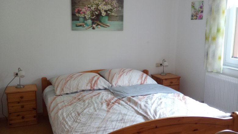 FW "Meadows & Fields", © Blumentalhof Bedroom with wooden bed, bedside tables and flower pictures on the wall.
